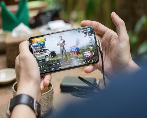 Mobile gaming demonstration shown on a secondary smartphone screen featuring beginner-friendly controls